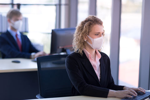 Business woman with curly blonde hair wearing a mask sitting in